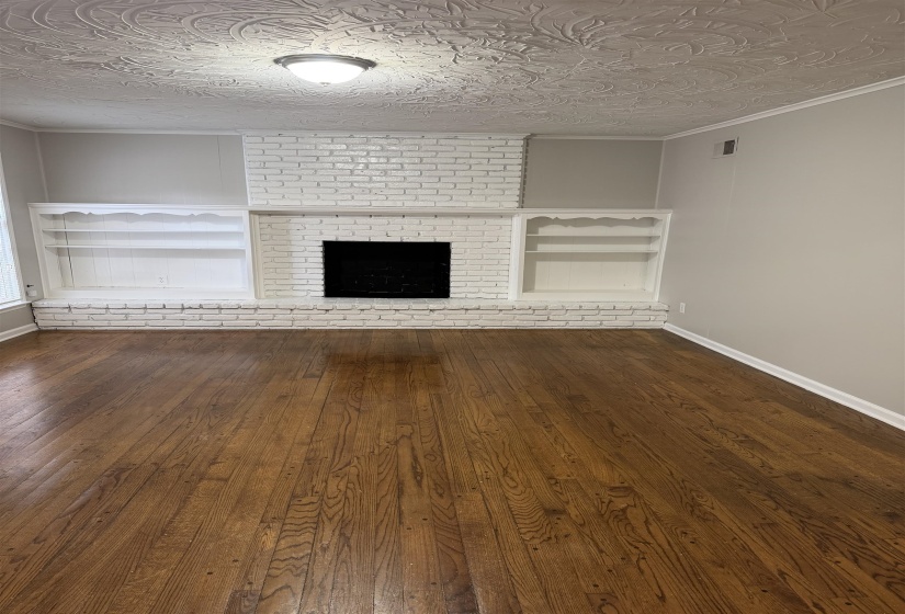 Living space featuring wood-finish flooring, a white-painted brick fireplace, built-in shelving, crown molding, and an ornate ceiling