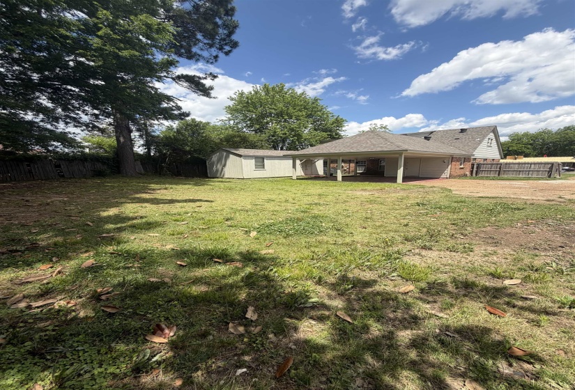 Expansive backyard with a covered patio featuring a shingled roof and brick-patterned flooring