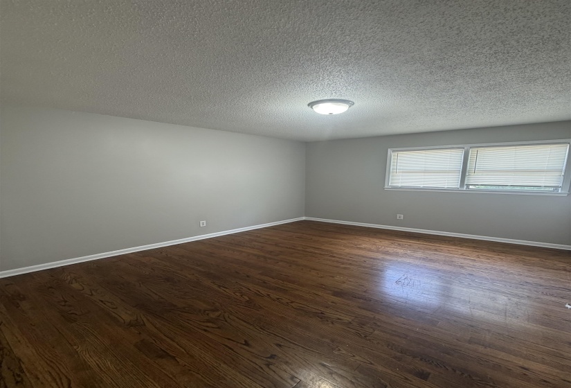 Spacious room featuring wood-finish flooring, light gray wall paint, white baseboards, and a semi-flush mount ceiling light fixture