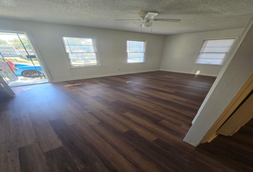 Spacious room featuring wood-finish flooring, light-colored walls, multiple windows, and a ceiling fan