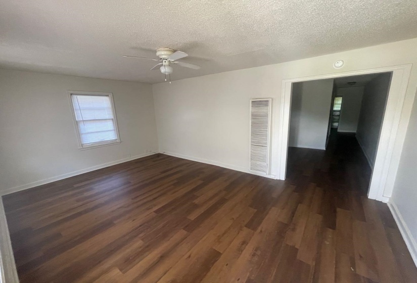 Spacious room featuring wood-finish flooring, light-toned walls, a ceiling fan, and a single window with blinds