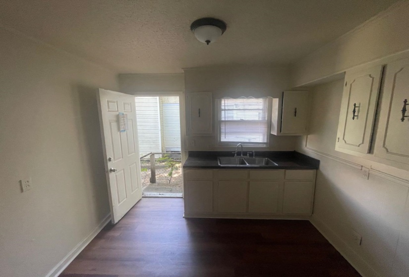 Compact kitchen space featuring wood-finish flooring, white cabinetry, dark countertops, and a double basin sink beneath a window