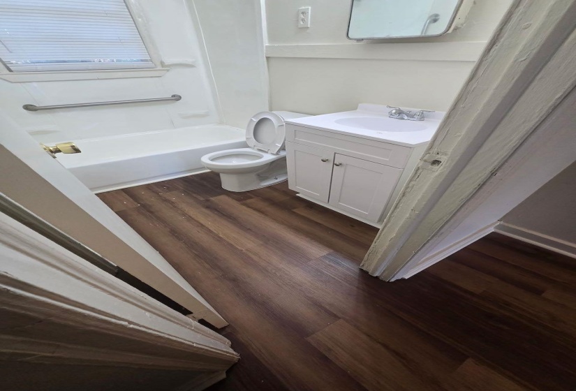Bathroom featuring a white vanity with integrated sink, white toilet, and tub with grab bar