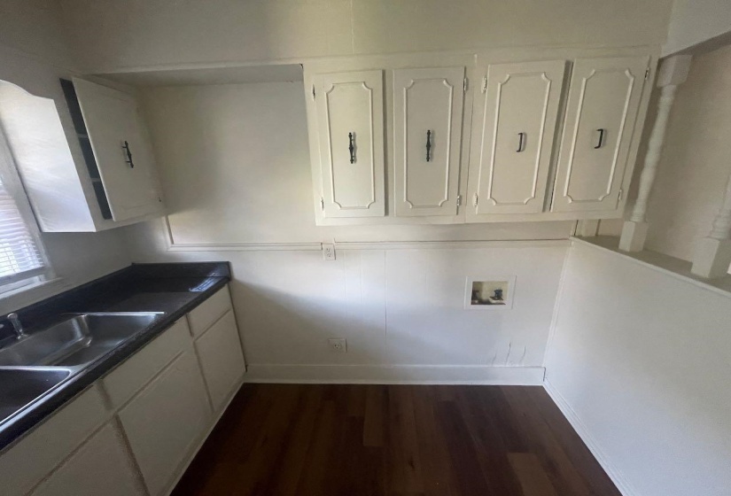 Kitchenette featuring a double basin stainless steel sink, dark countertop, and white cabinetry