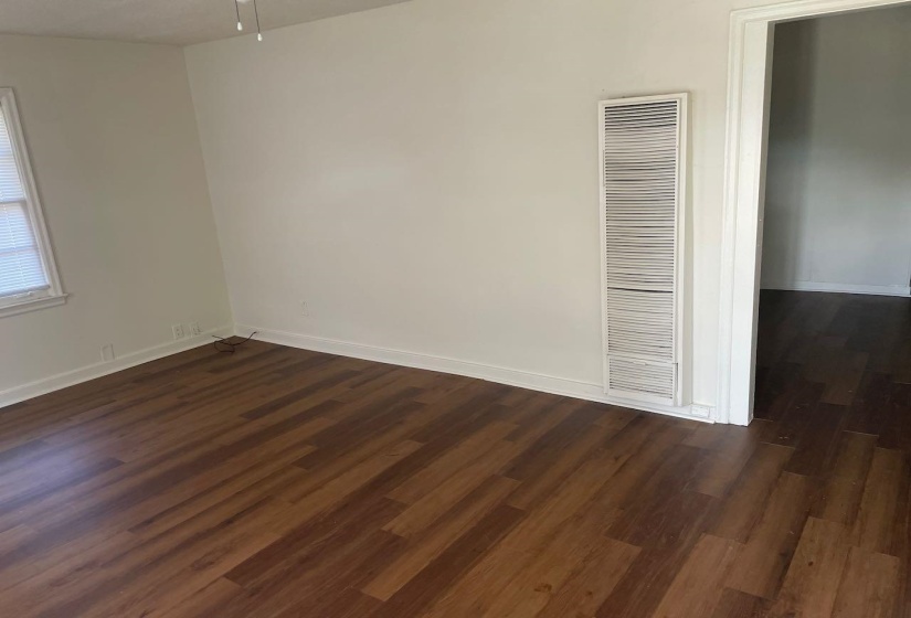Spacious room featuring wood-finish flooring, white baseboards, and a window with blinds