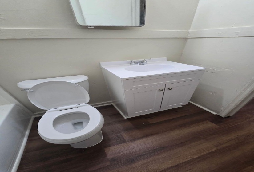 Updated bathroom featuring a new white vanity with integrated sink, chrome faucet, and wood-finish flooring