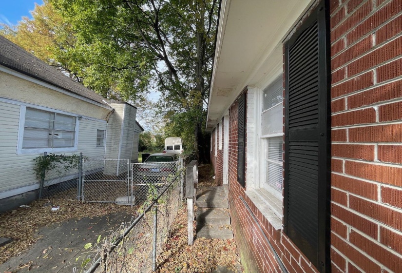 Brick exterior with black louvered shutters, white window trim, and a concrete walkway