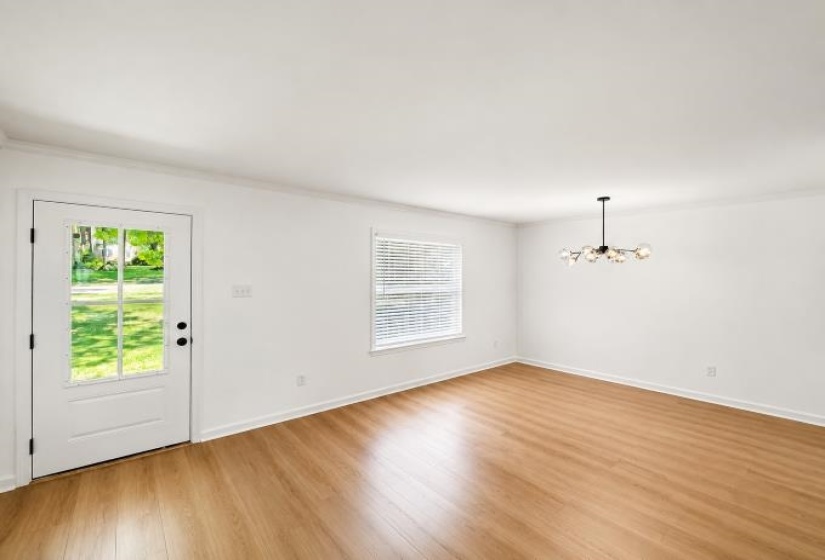 Open-concept room featuring wood-finish flooring, white walls, and a contemporary chandelier