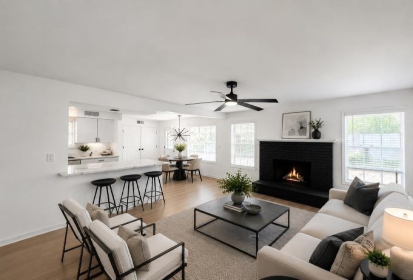 Open-concept living space featuring wood-finish flooring, a contemporary fireplace with a black brick surround, multiple windows, and a ceiling fan