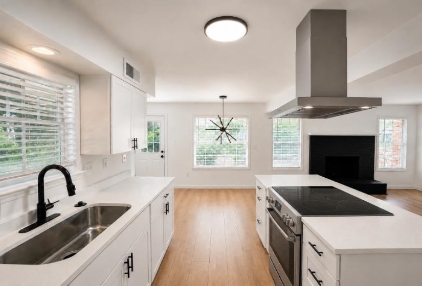 Open-concept kitchen featuring white cabinetry, light-toned wood-finish flooring, and a central island with an integrated cooktop and oven