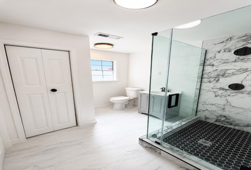 Contemporary bathroom featuring a spacious glass-enclosed shower with black hexagonal tile flooring and marbled wall tiling