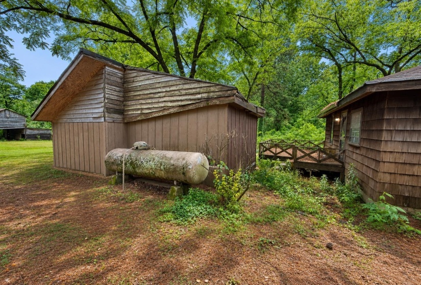 Wood-sided outbuilding with a gable roof and visible propane tank