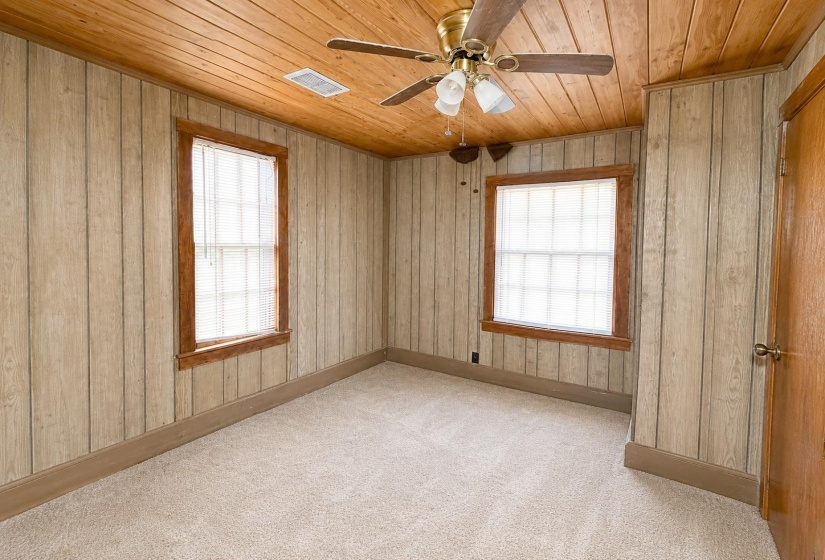 Carpeted room featuring two windows with blinds, wood trim, and light wood-paneled walls