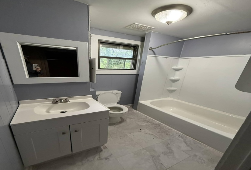 Full bathroom featuring a white vanity with integrated sink, coordinating wall-mounted medicine cabinet, white bathtub with shower surround, and light-toned tile flooring