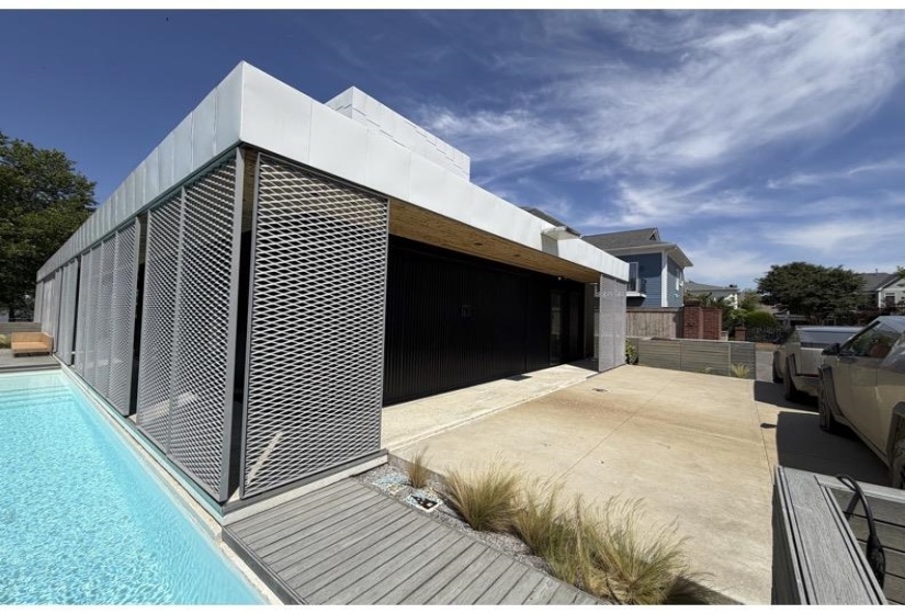 Modern exterior featuring a swimming pool, architectural screening, a dark-toned garage door, a concrete driveway, and minimalist landscaping with ornamental grasses