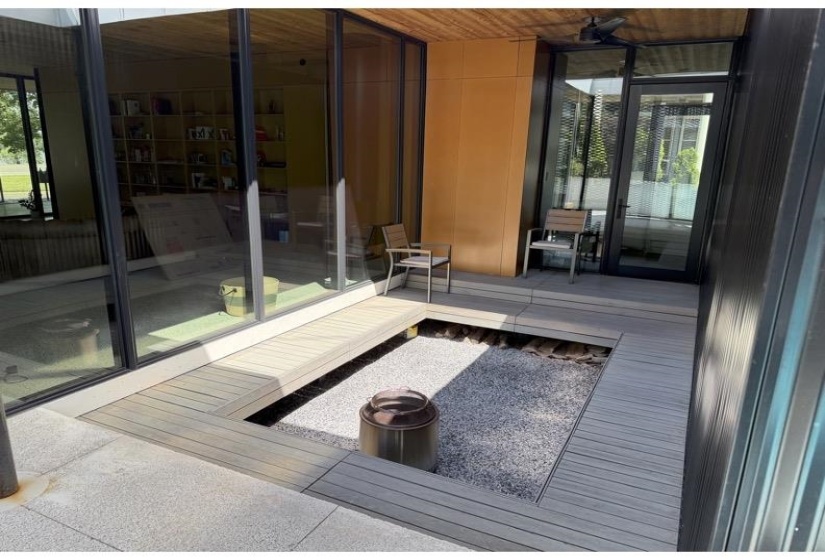 Outdoor living area featuring a built-in wood-finish deck with integrated gravel bed, full-height glass panels, and a ceiling fan