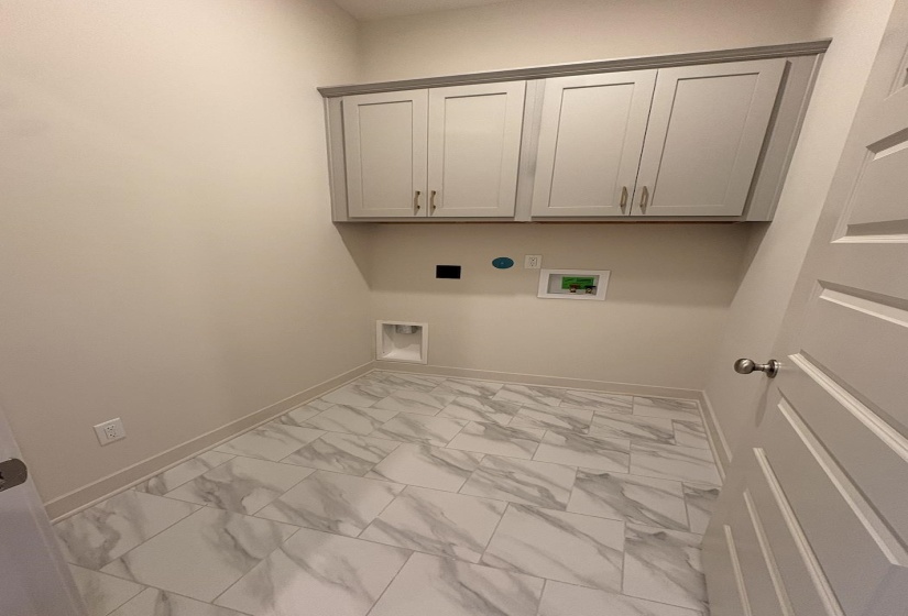 Laundry room featuring light gray cabinetry with brushed nickel hardware, a white tile floor with gray veining, and a paneled interior door