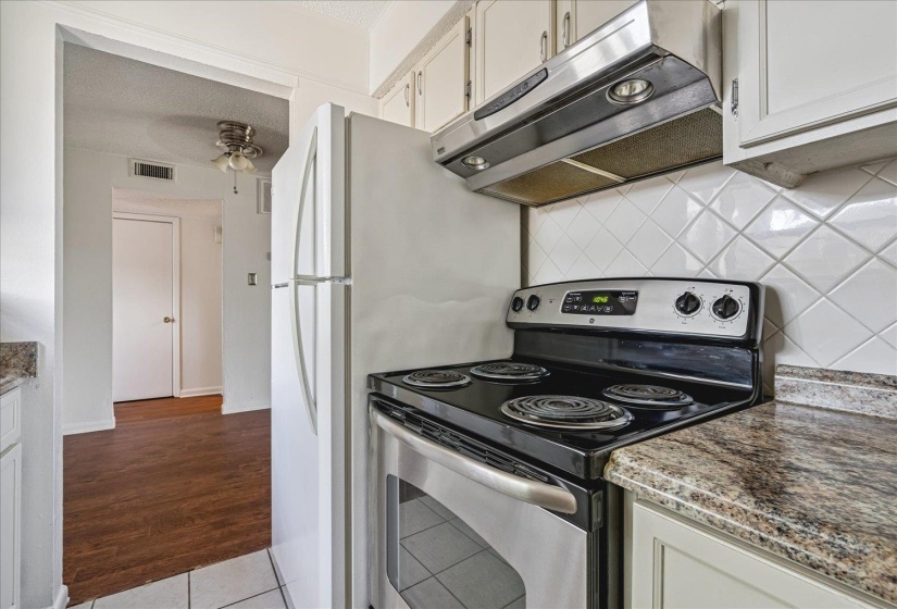 Kitchen featuring a stainless steel range with overhead ventilation, white cabinetry, and granite-look countertops