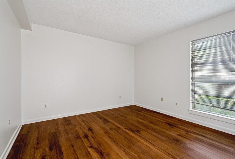 Spacious room featuring wood-finish flooring, white walls, and a window with horizontal blinds