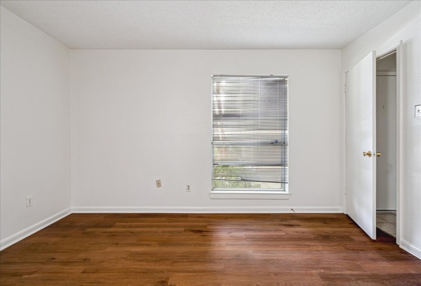 Spacious room featuring wood-finish flooring, crisp white walls, and a window with horizontal blinds