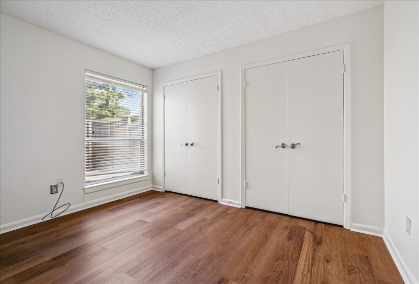 Bedroom with wood-finish flooring, a large window featuring horizontal blinds, and two sets of double-door closets