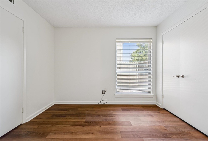 Room featuring wood-finish flooring, white baseboards, a window with horizontal blinds, and two white bi-fold closet doors