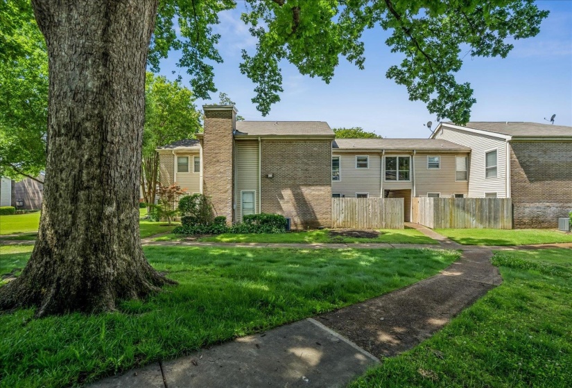 Exterior featuring brick and siding construction, mature trees, a privacy fence, and a concrete pathway