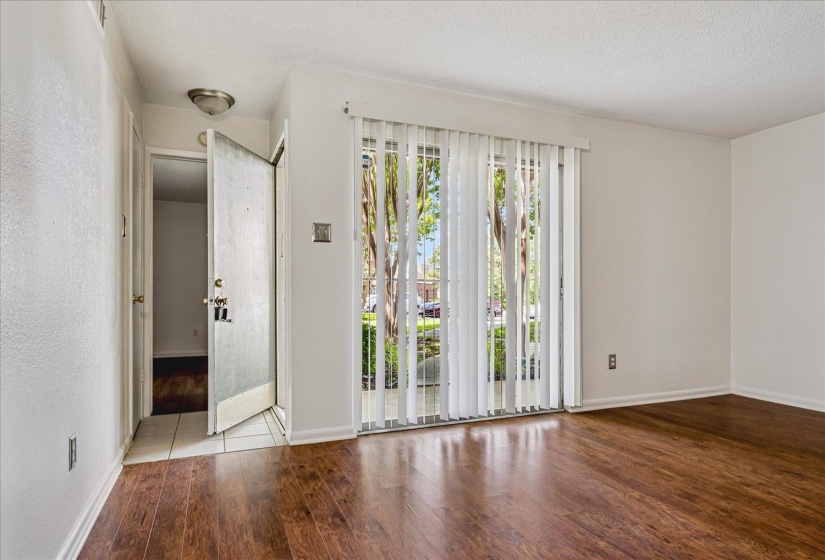 Living area with wood-finish flooring, white walls, and a sliding glass door with vertical blinds