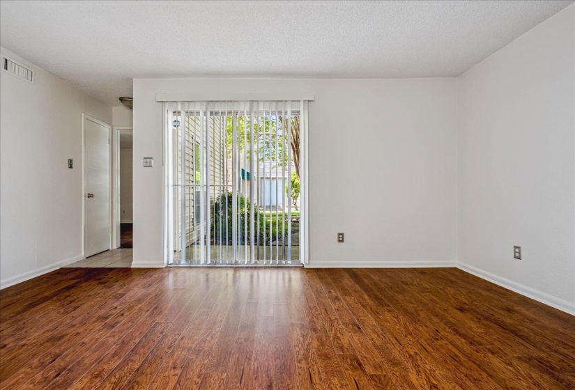 Spacious interior featuring wood-finish flooring, white walls, and a sliding glass door with vertical blinds