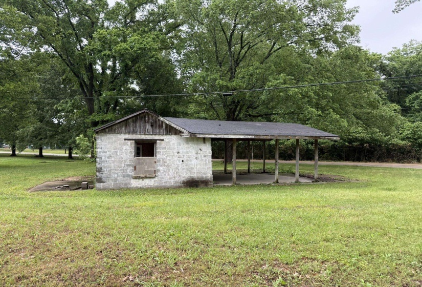 Block construction utility building featuring a covered carport structure and a dark shingle roof