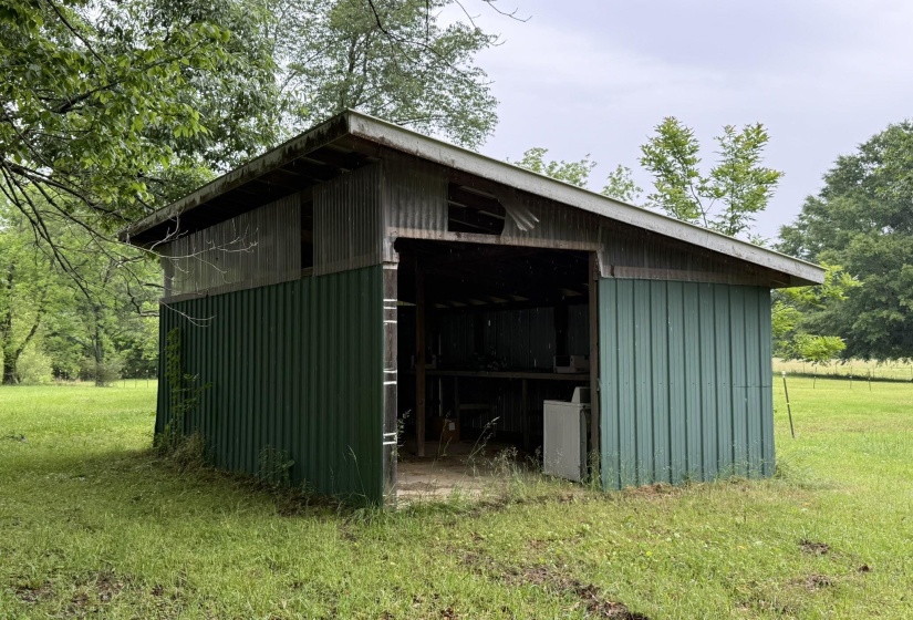 Metal-sided utility shed with an open-air bay, corrugated metal roofing, and a gravel base