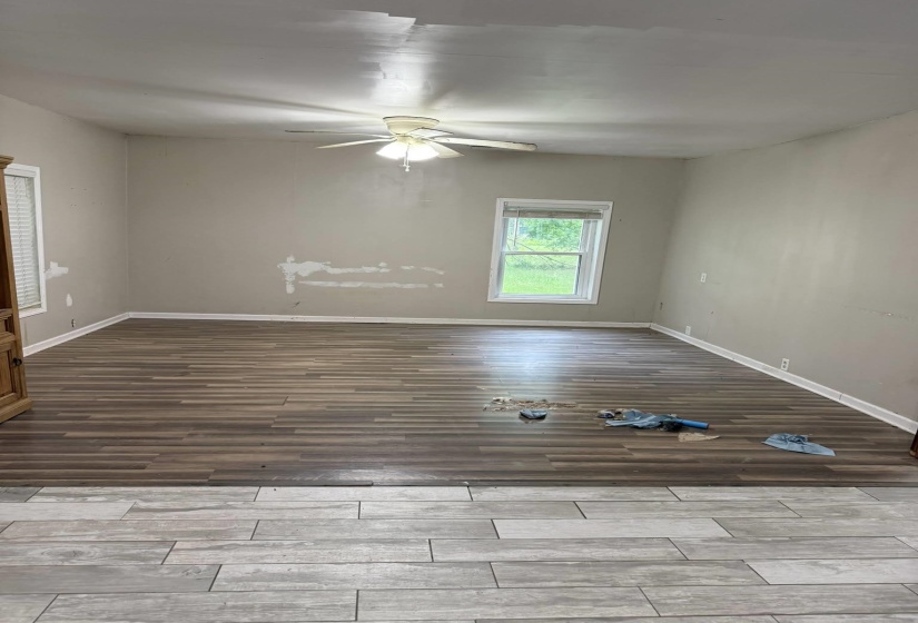 Expansive room featuring wood-finish flooring, a ceiling fan with integrated lighting, and white baseboards