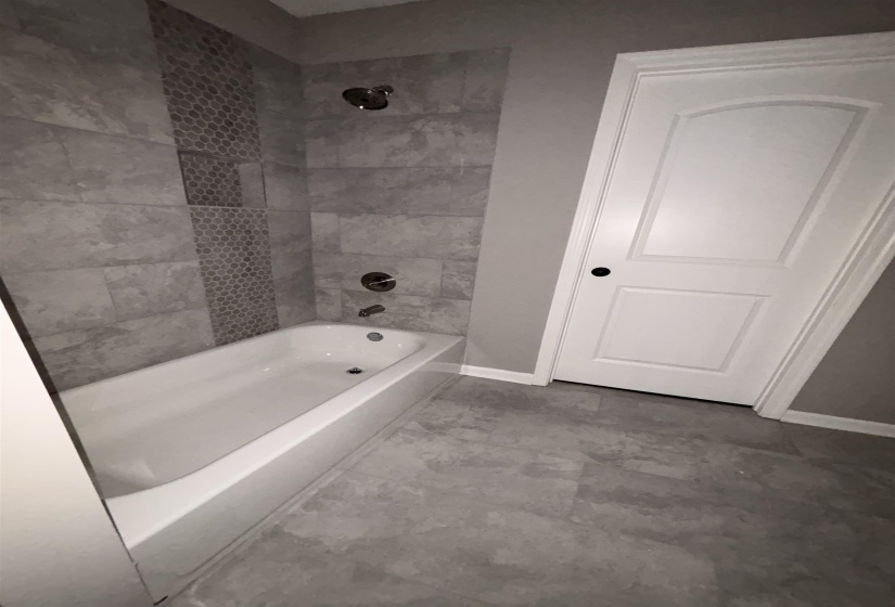 Bathtub and shower combination featuring gray tile surround with a vertical mosaic accent stripe and recessed shower niche
