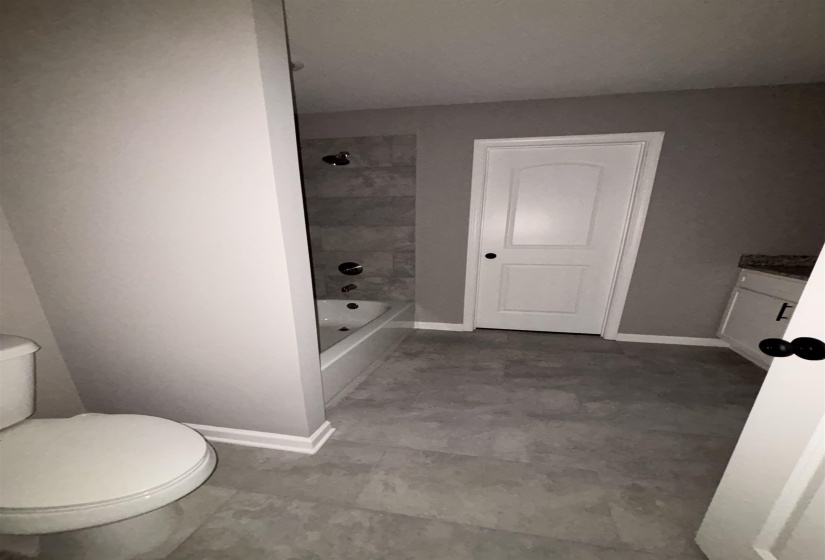 Bathroom featuring a white bathtub with dark fixtures, grey tiled shower surround, and grey plank flooring