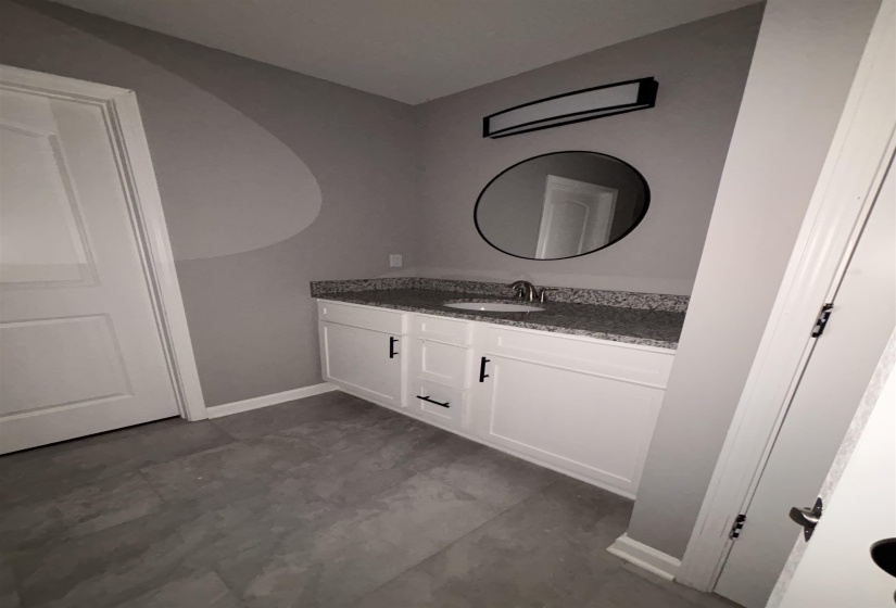 Bathroom vanity with a granite countertop, undermount sink, and dark hardware
