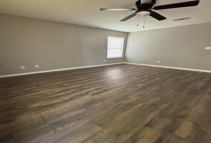 Spacious room featuring wood-finish flooring, neutral-toned walls, a ceiling fan with integrated lighting, and a single window with blinds