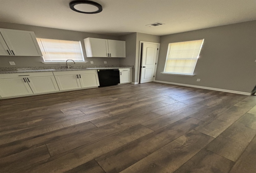 Kitchen featuring wood-finish flooring, white cabinetry with dark hardware, a stainless steel sink with a gooseneck faucet, light-toned countertops, and a black dishwasher