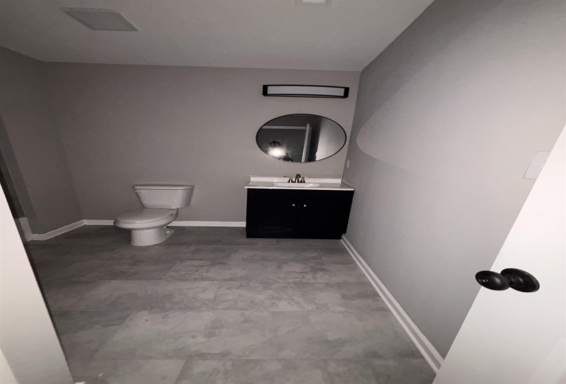 Bathroom featuring gray wall paint, a black vanity with a white countertop, a circular mirror, and tile flooring