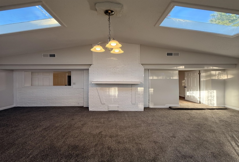 Living area featuring vaulted ceilings with two skylights, a white brick fireplace, and dark gray carpeting