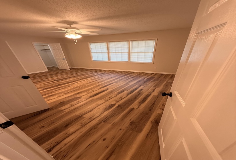 Spacious room featuring wood-finish flooring, ample natural light from multiple windows, and a ceiling fan with integrated lighting