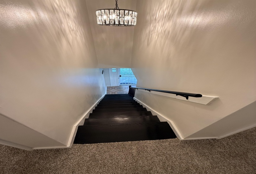 Modern drum chandelier illuminating a carpeted landing and dark wood-finish stairs with a contrasting black handrail