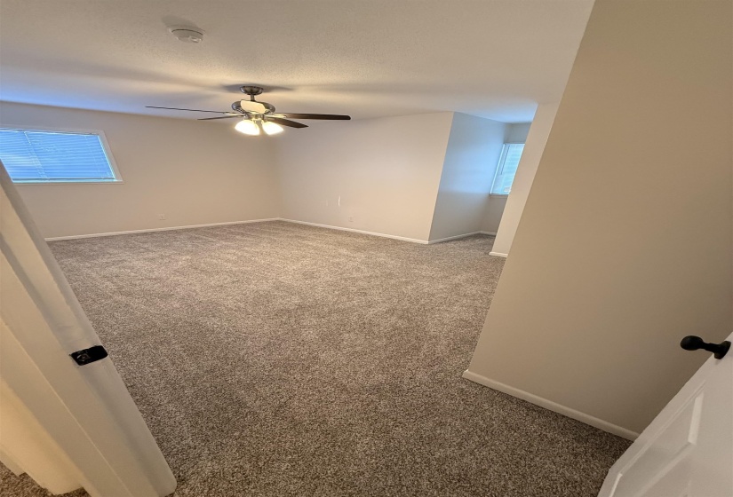 Spacious room featuring neutral carpeting, light-toned walls, and a ceiling fan with integrated lighting