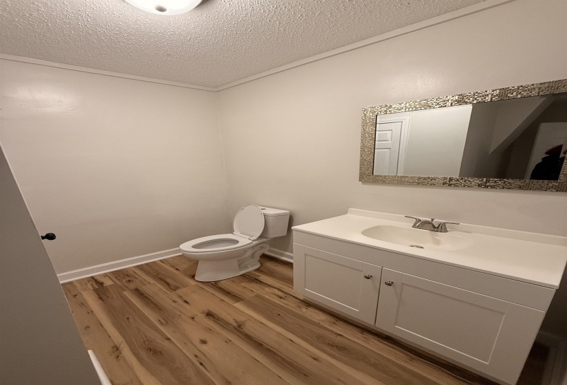 Bathroom featuring wood-finish flooring, white vanity with integrated sink, chrome faucet, and a decorative framed mirror