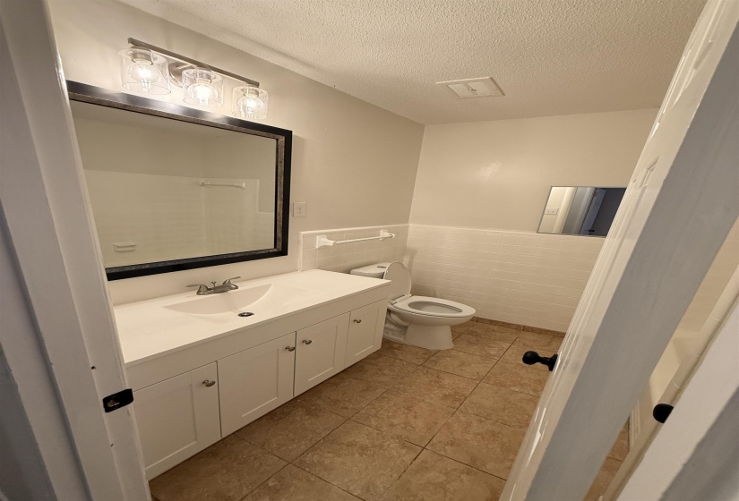 Bathroom featuring a white vanity with integrated sink, coordinating white subway tile wainscoting, a wall-mounted mirror, and tiled flooring