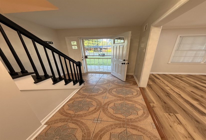 Foyer featuring patterned tile flooring, a white paneled entry door with a security screen, and a staircase with black railings