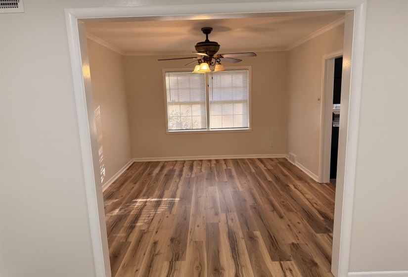 Open room featuring wood-finish flooring, two windows with blinds, a ceiling fan with integrated lighting, and crown molding