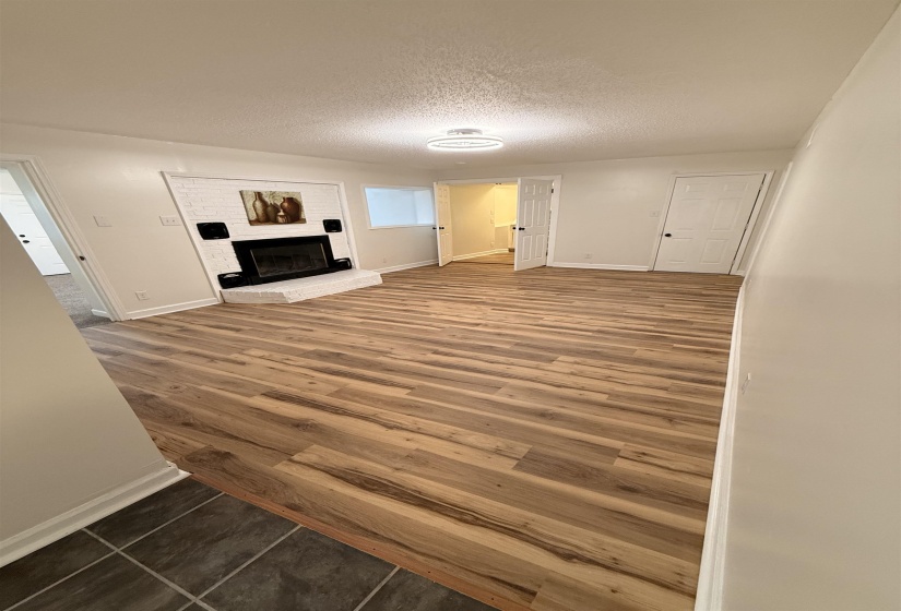 Spacious room featuring wood-finish flooring, a white brick fireplace with a raised hearth, and multiple entryways