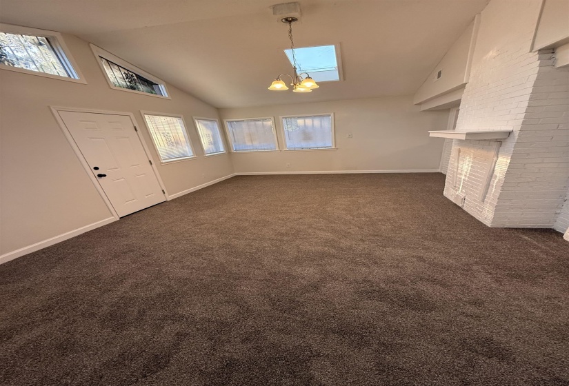 Spacious living area featuring a vaulted ceiling with a skylight, multiple windows, plush carpet, and a brick fireplace with a mantle