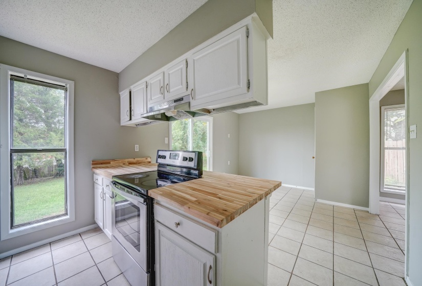 Kitchen featuring wood counters, stainless steel range with electric stovetop, white cabinetry, light tile patterned flooring, and a textured ceiling