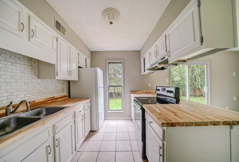 Kitchen with stainless steel range with electric stovetop, a textured ceiling, light tile patterned floors, freestanding refrigerator, and plenty of natural light